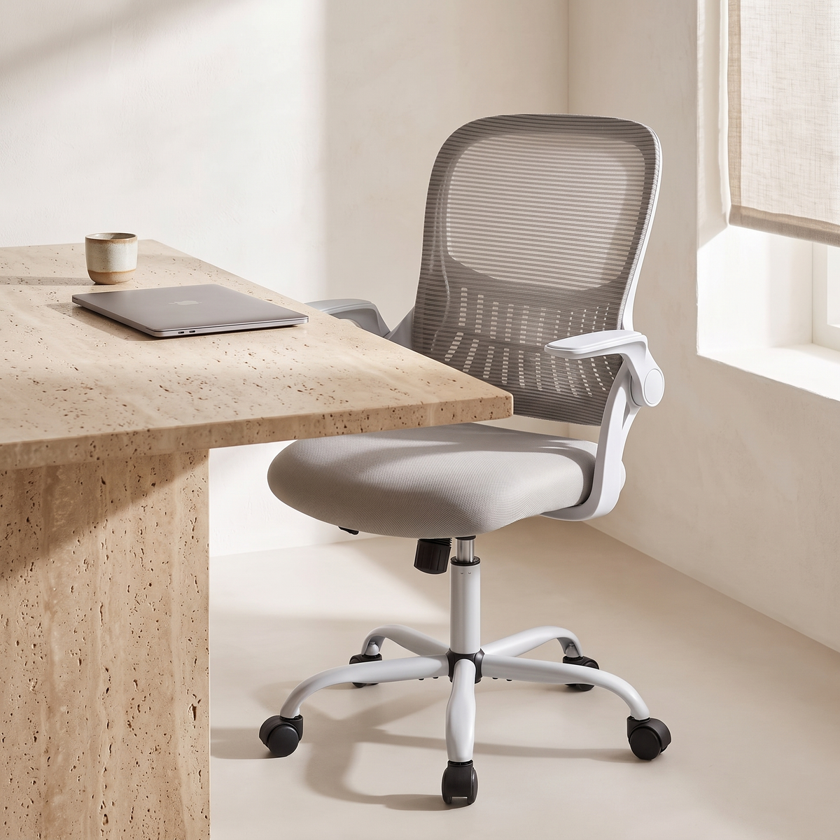 Chaise Ergonomique Essentiel — Gris — devant un bureau en travertin, lumière du matin